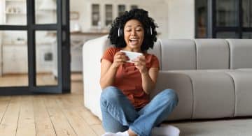 Excited Black Woman Playing Video Games On Smartphone At Home