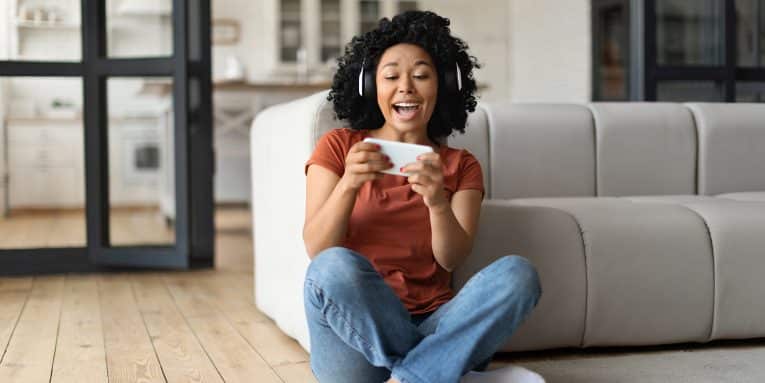 Excited Black Woman Playing Video Games On Smartphone At Home